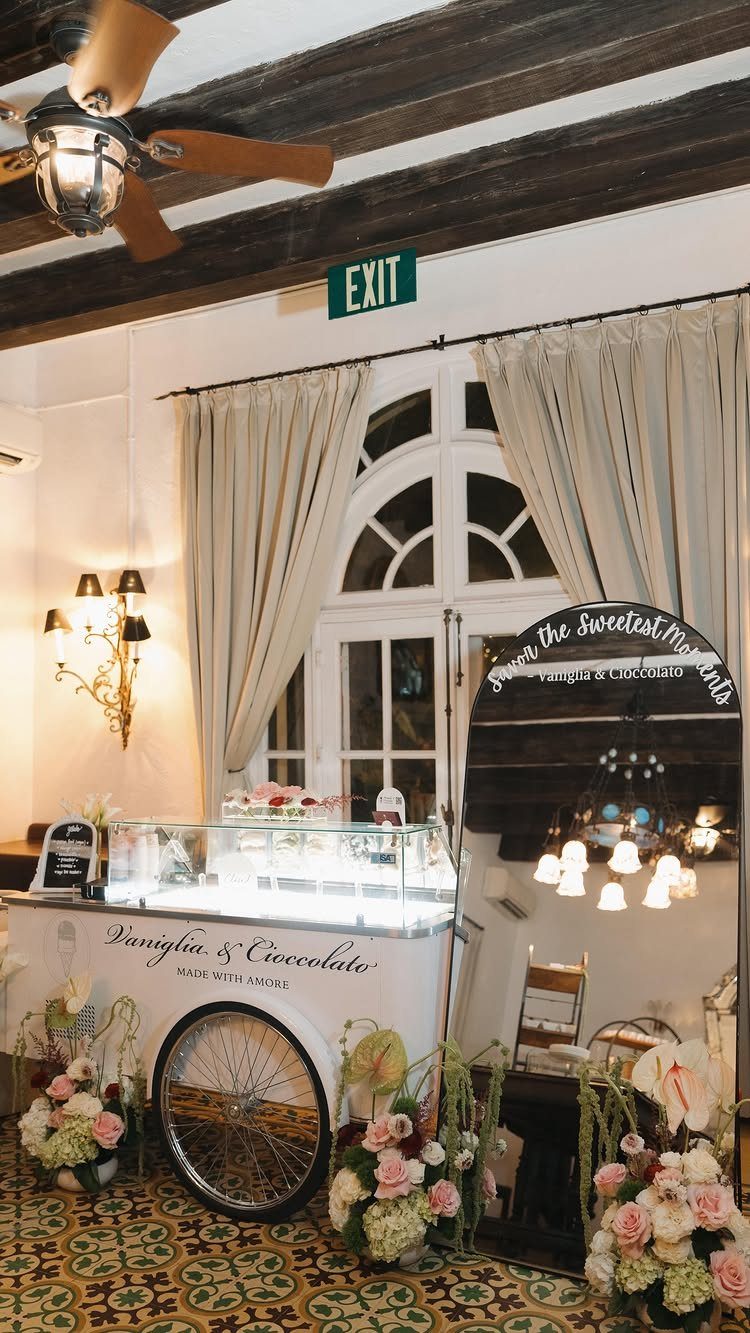 Vintage white gelato cart with floral decorations and glass display in an elegant room.