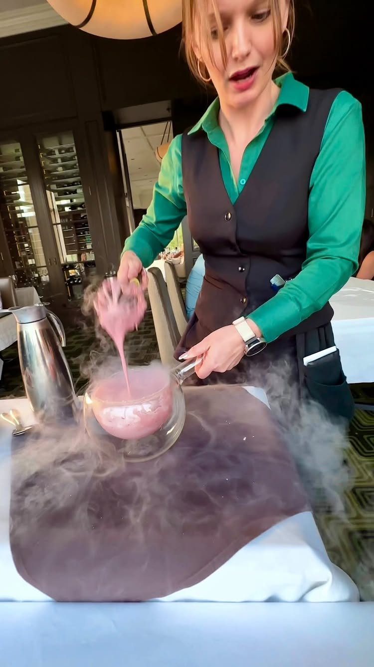 Woman preparing a pink dessert with liquid nitrogen vapor flowing over a table.