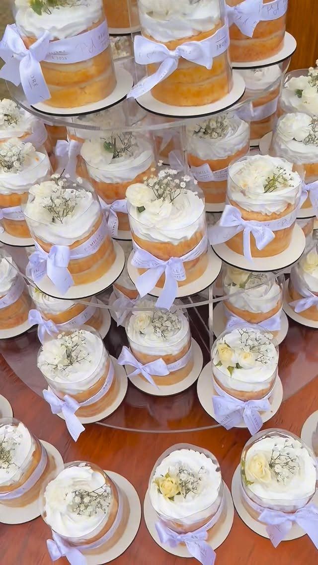 Mini layer cakes with white frosting and purple ribbons on tiered acrylic stands.