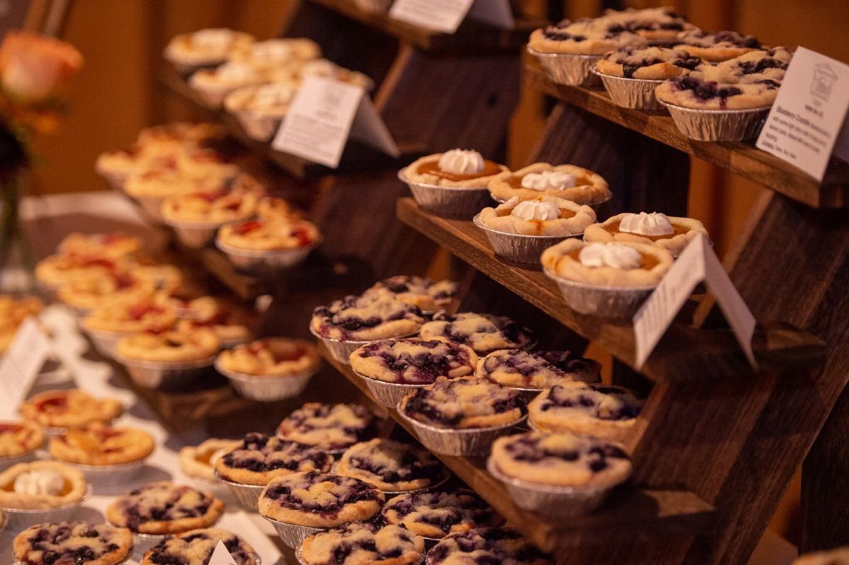 Mini pies with various fruit fillings displayed on tiered dark wooden shelves.