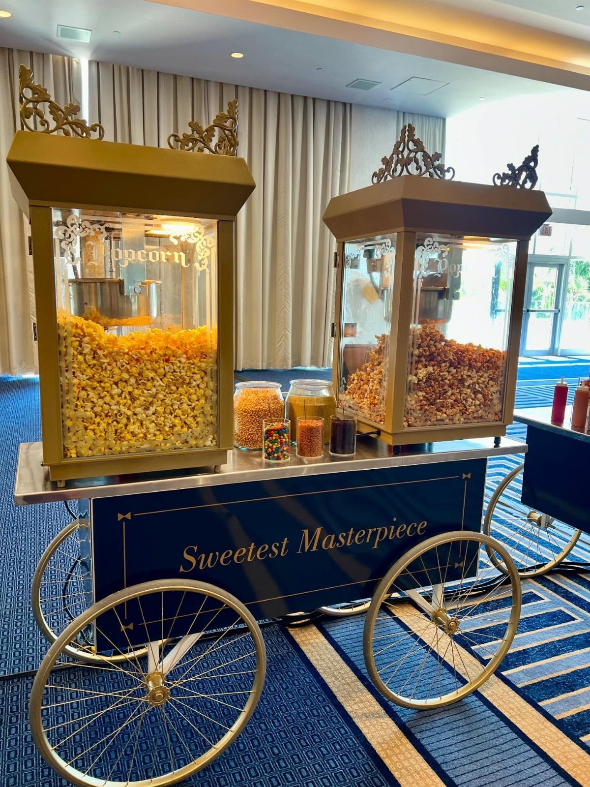 Popcorn cart with gold dispensers and navy blue base on a blue carpet.