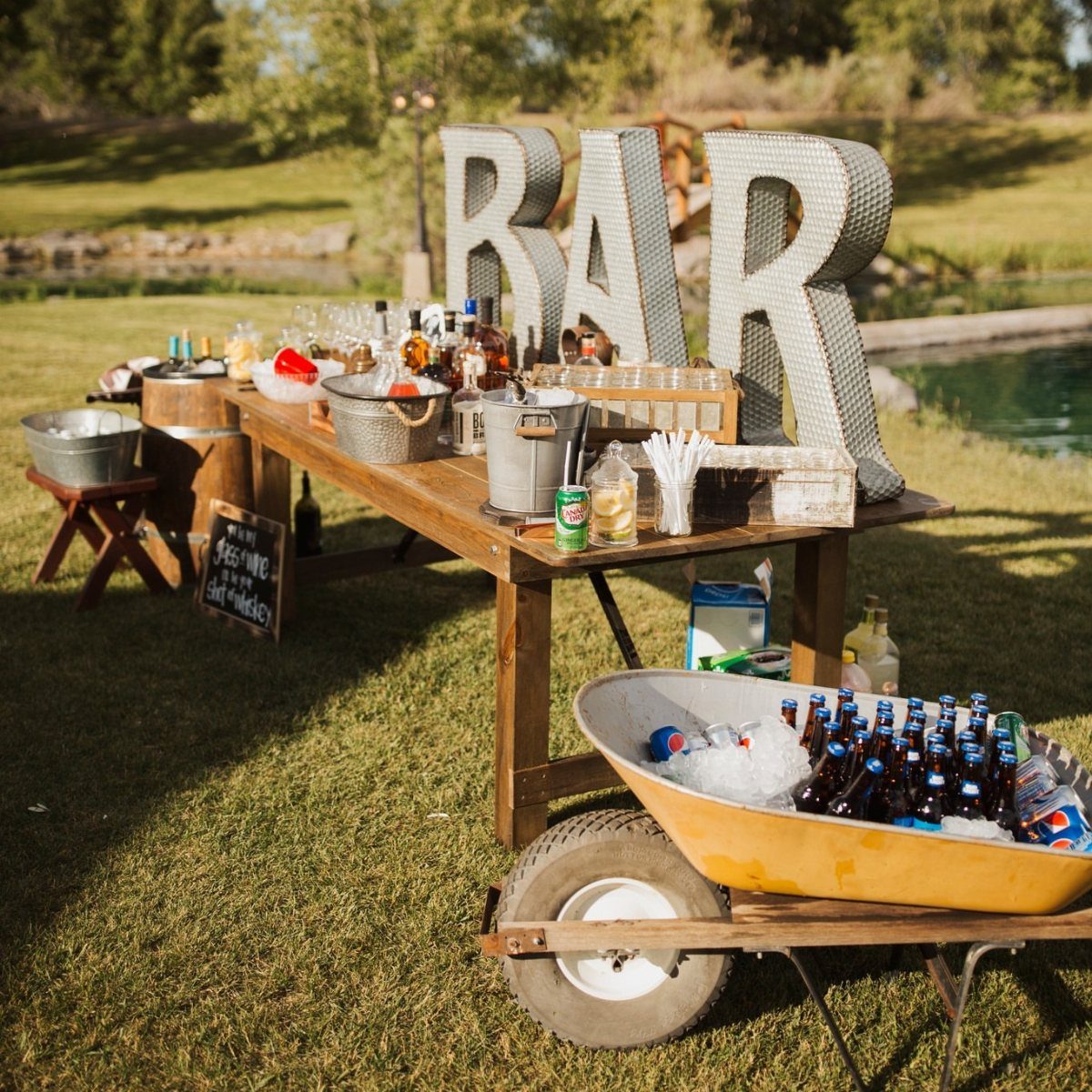 Outdoor wooden bar setup with liquor bottles and beer in a wheelbarrow