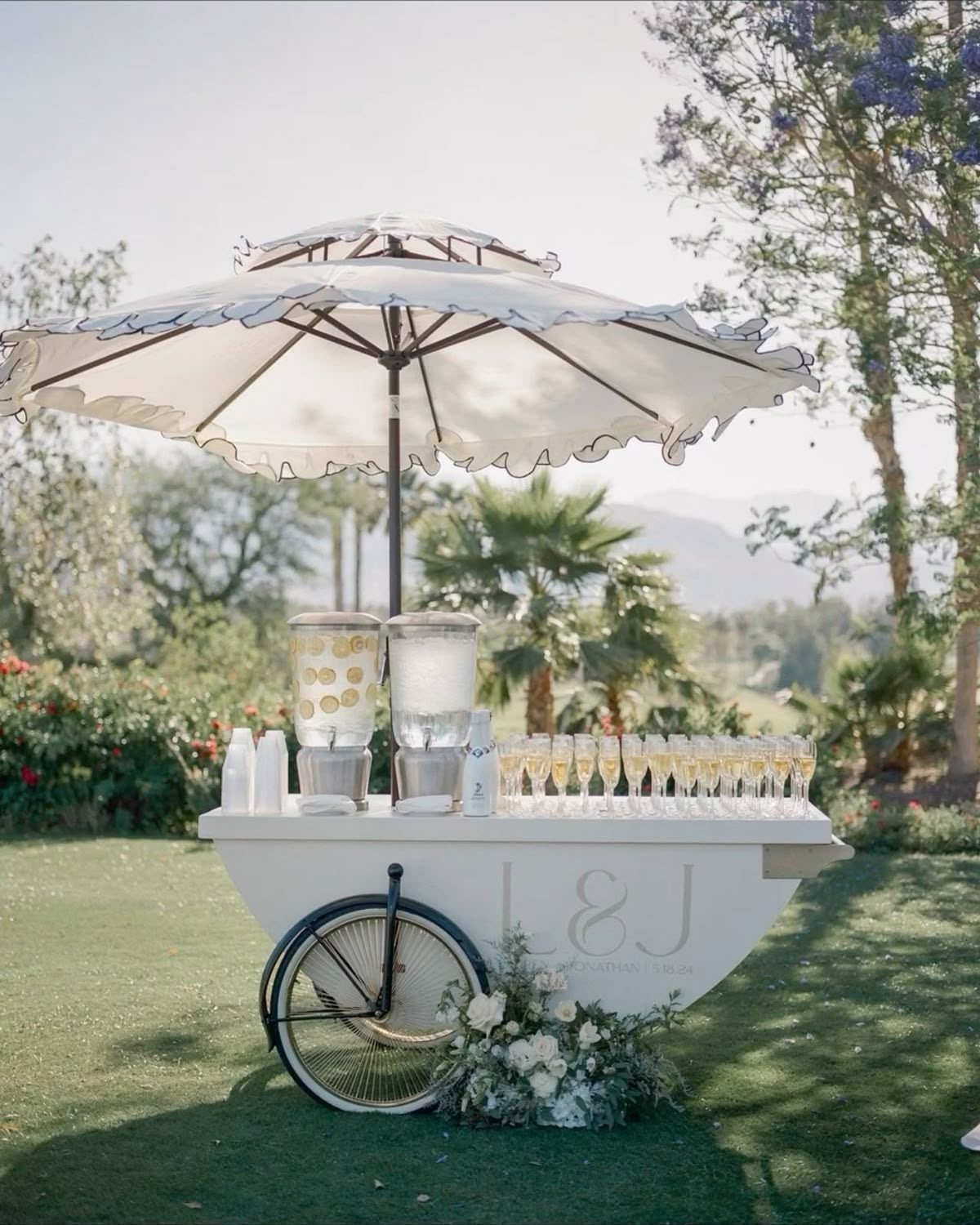 White mobile drink cart with umbrella and champagne glasses on a sunny lawn