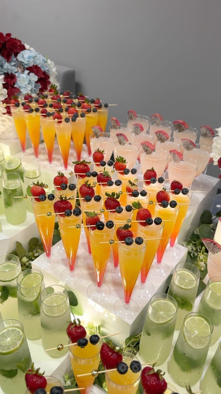 Colorful wedding drinks with fruit garnishes arranged on white tiered display stands.