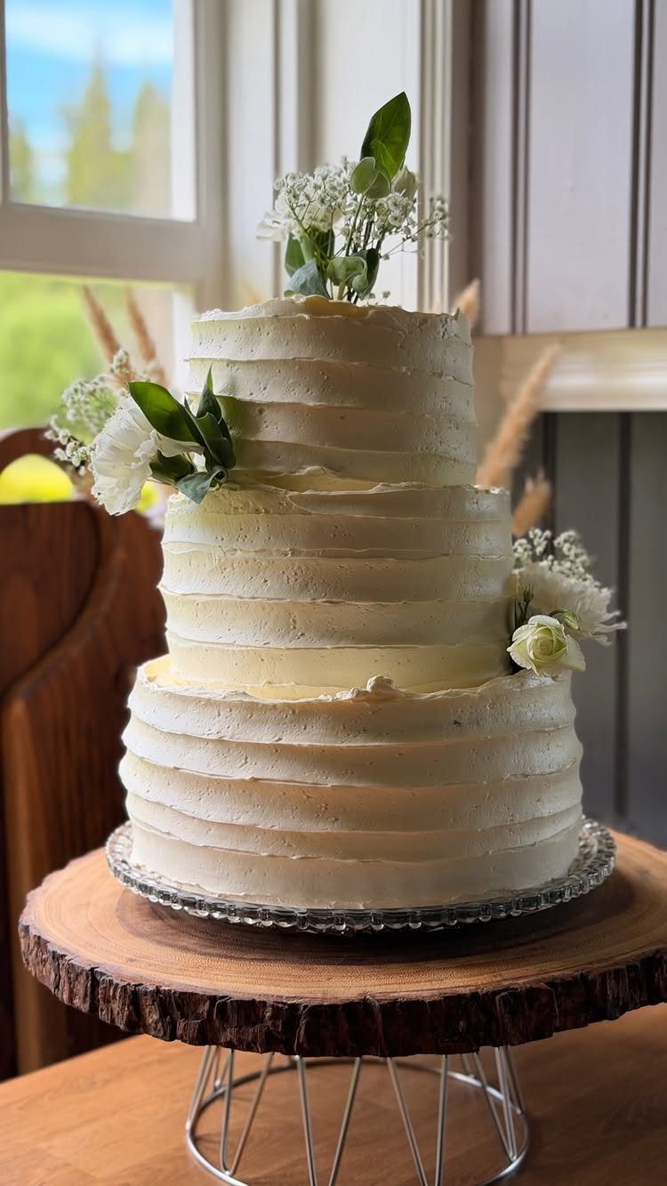 Three-tier white buttercream cake with ridged frosting and delicate floral accents on wood.