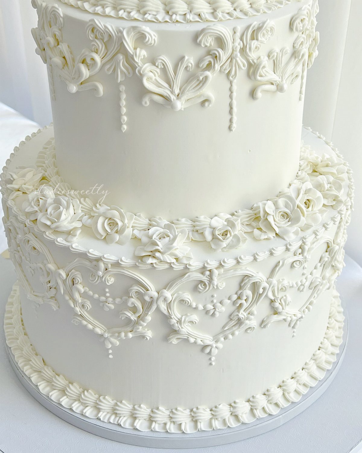 Two-tier white wedding cake decorated with intricate icing scrolls and frosting roses.