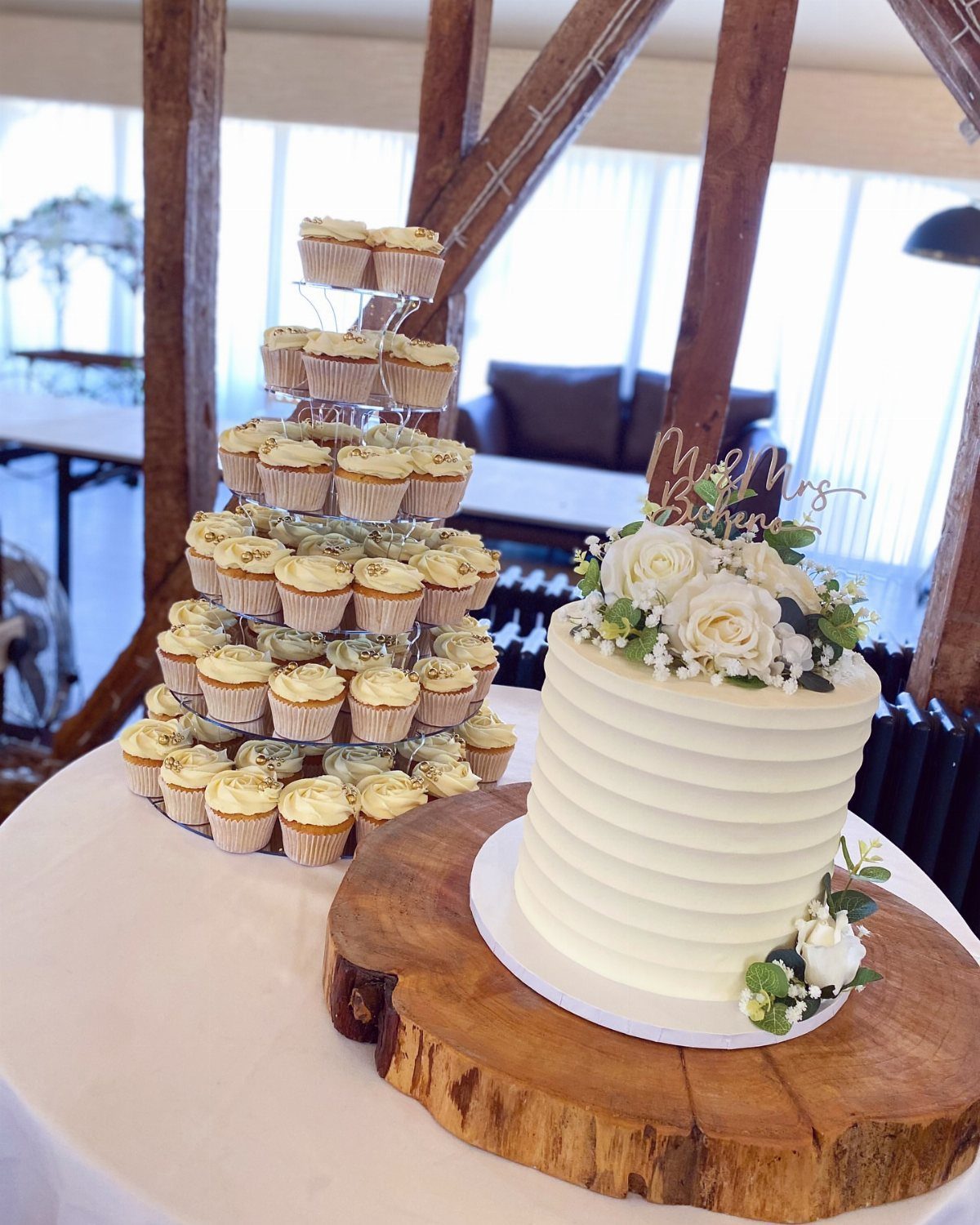 White textured wedding cake with roses and a tower of cupcakes on a table
