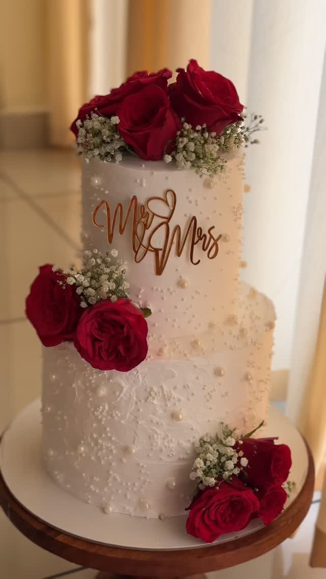 Two-tier white wedding cake decorated with red roses and a gold Mr & Mrs topper