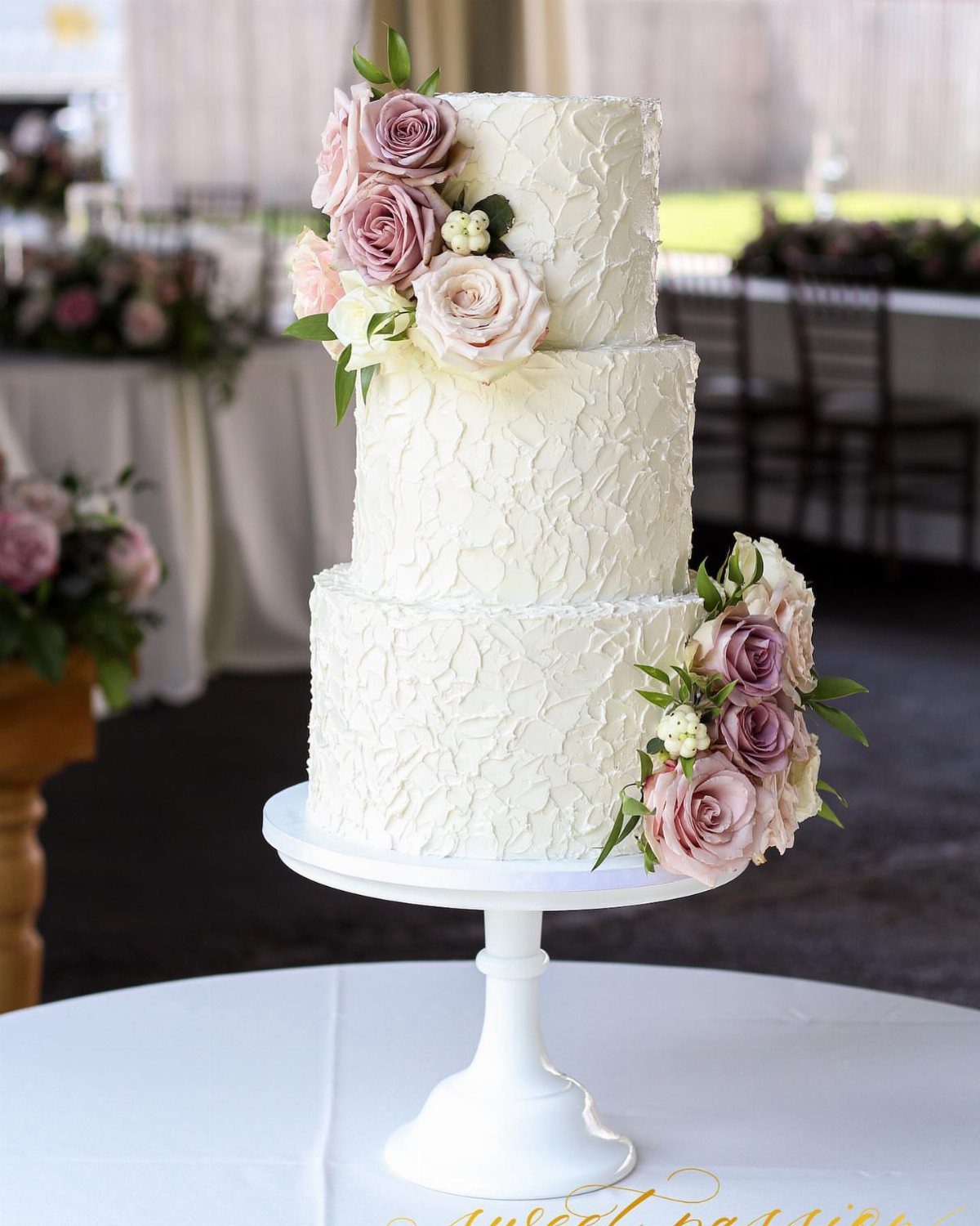 Three-tier white wedding cake with textured icing and dusty rose floral decorations.