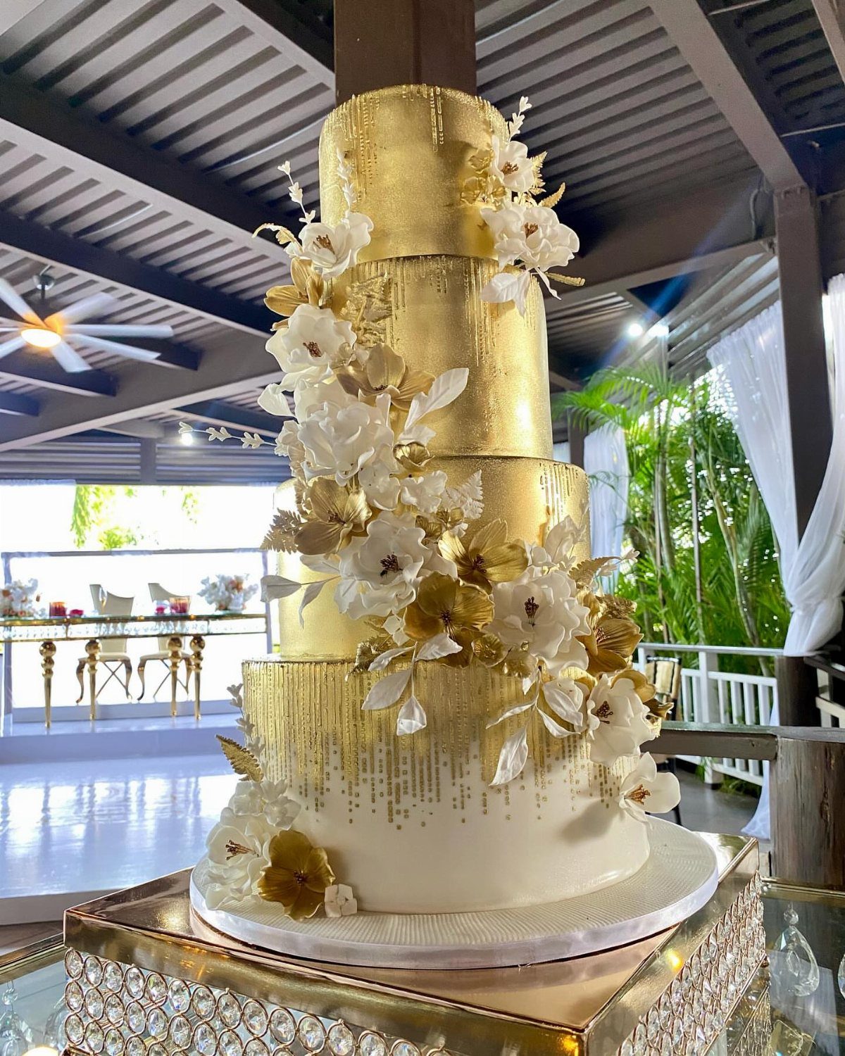 Multi-tiered gold and white wedding cake decorated with gold leaf and sugar flowers.