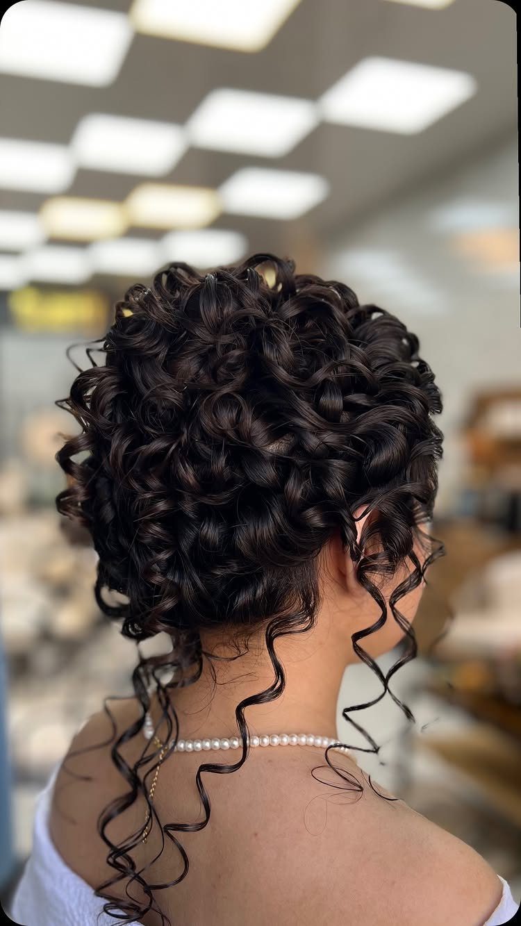 Dark curly hair styled in a voluminous bridal updo with loose ringlets.