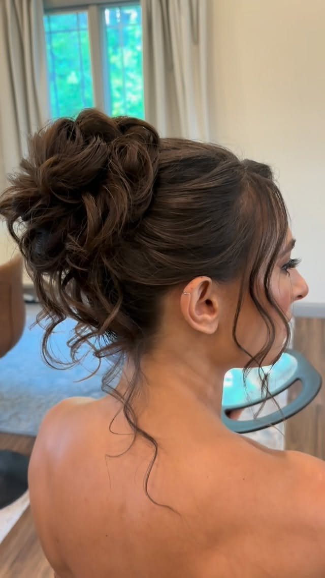 Woman with a loose textured brown hair bun and curly face-framing tendrils.