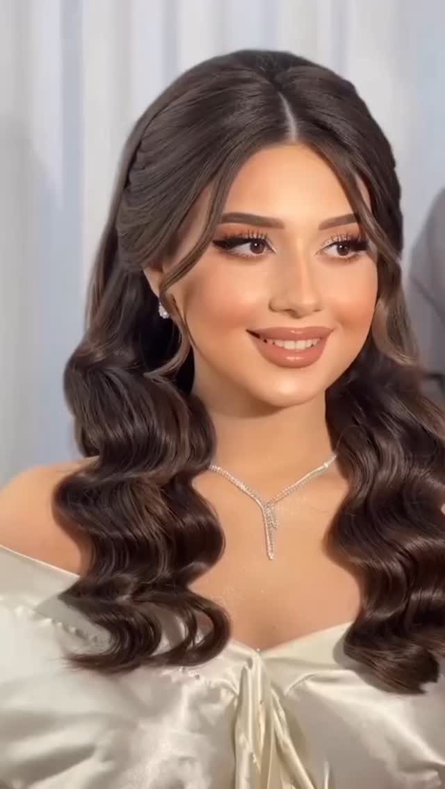 Woman with long dark brown hair styled in soft romantic waves and jewelry.