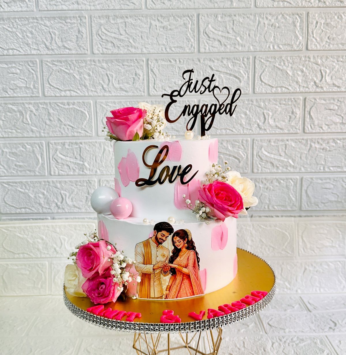Two-tier white engagement cake with pink roses and a couple's photo topper.