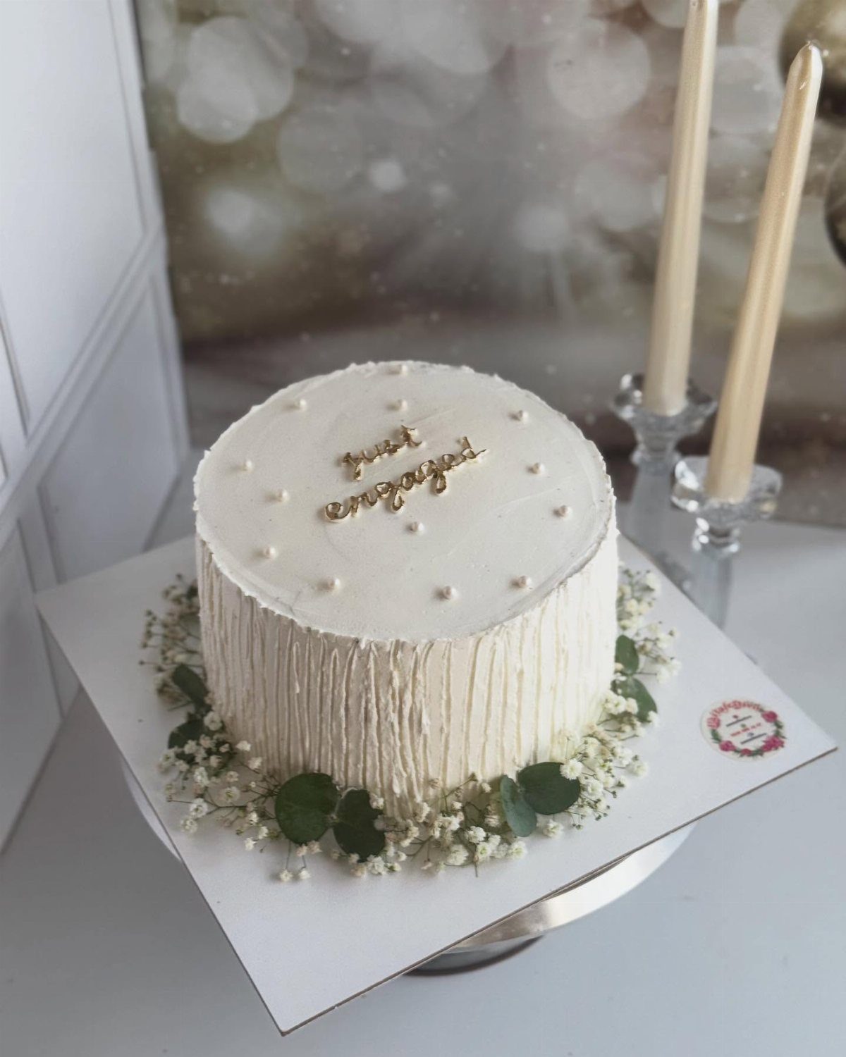 White frosted engagement cake with gold topper and baby's breath floral base.
