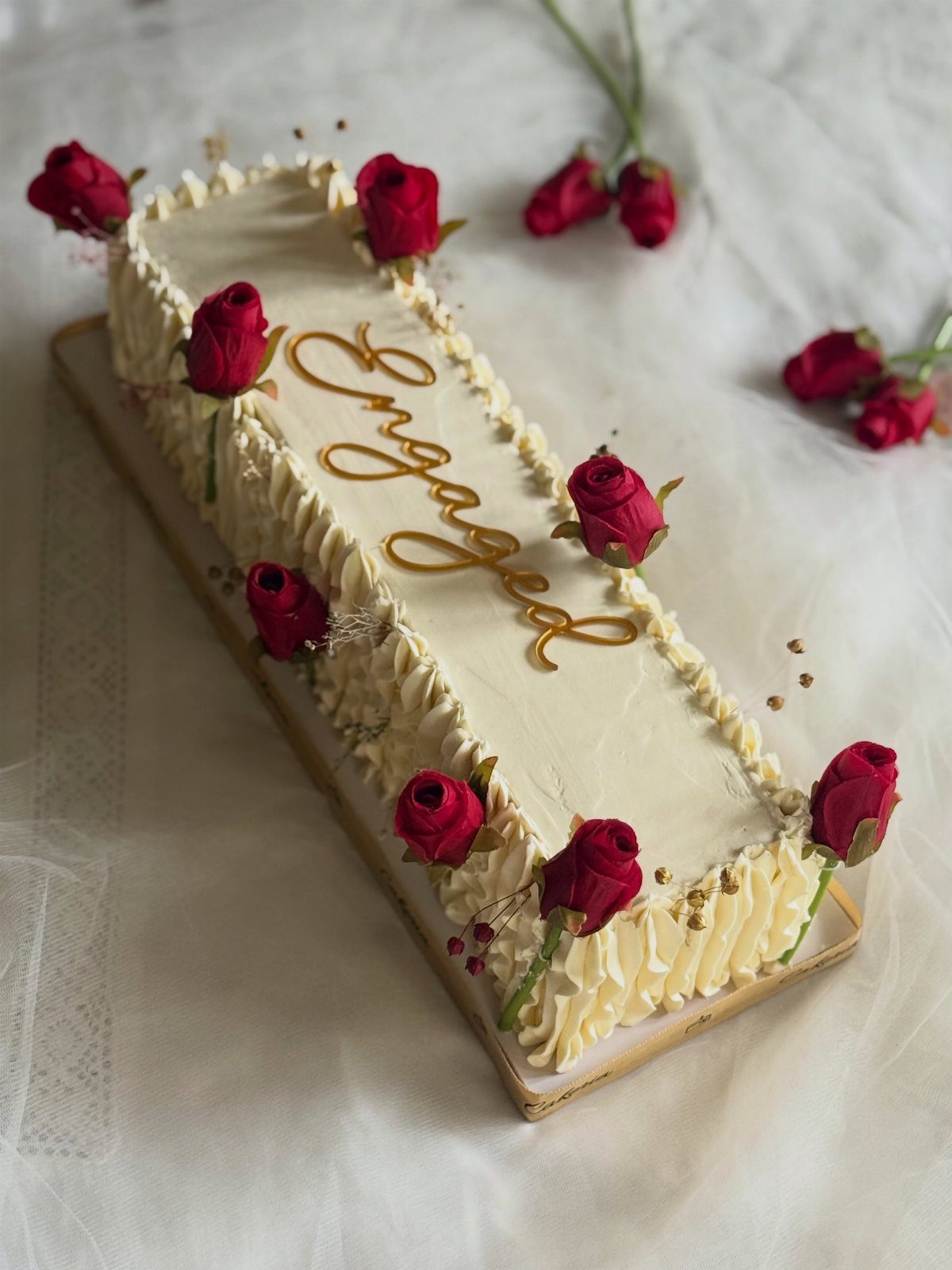 Rectangular white cake with red roses and gold Engaged lettering on white fabric
