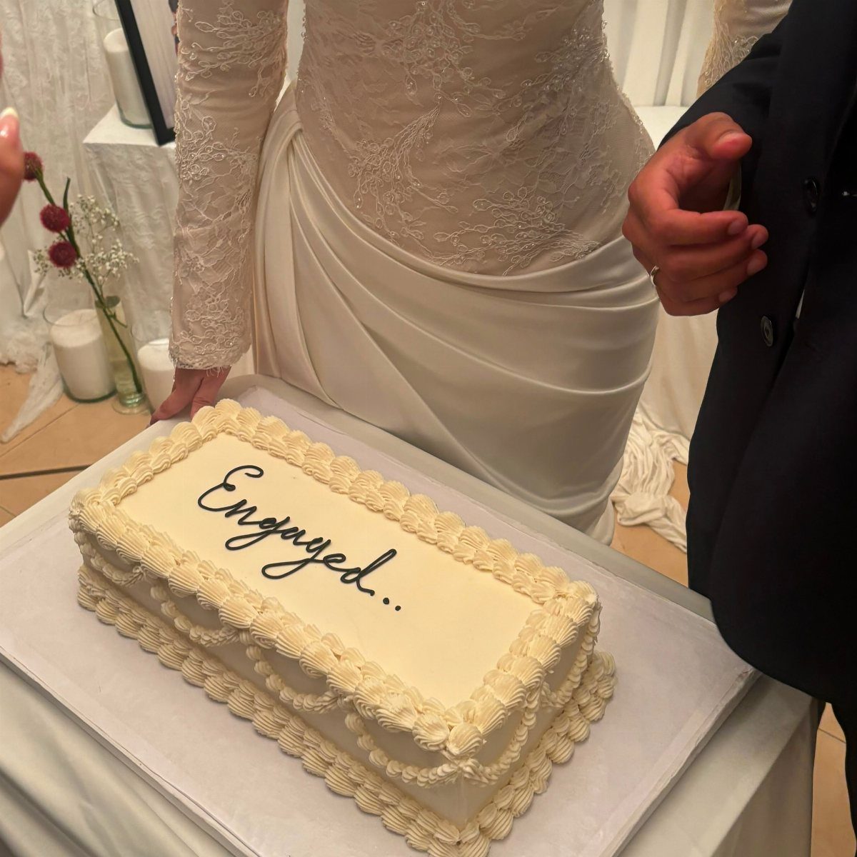 Rectangular white engagement cake with piped cream borders and black cursive text.