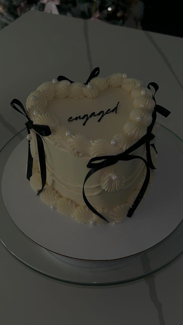 Heart-shaped white cake with black ribbons and 'engaged' written in cursive on top.