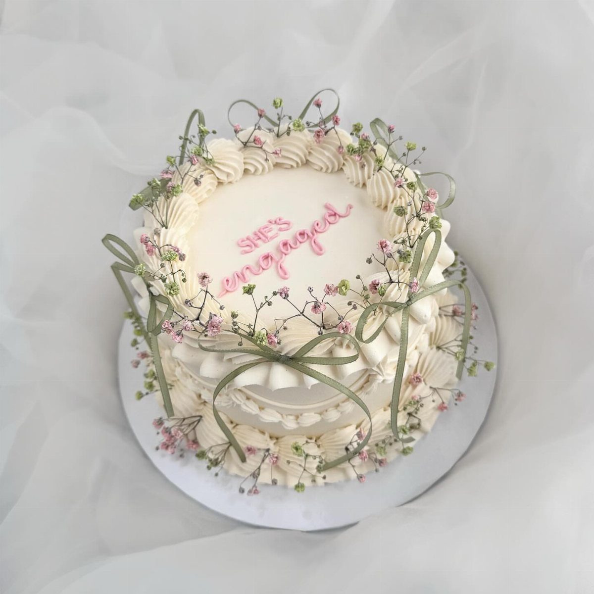 White engagement cake decorated with pink baby's breath flowers and green ribbons.