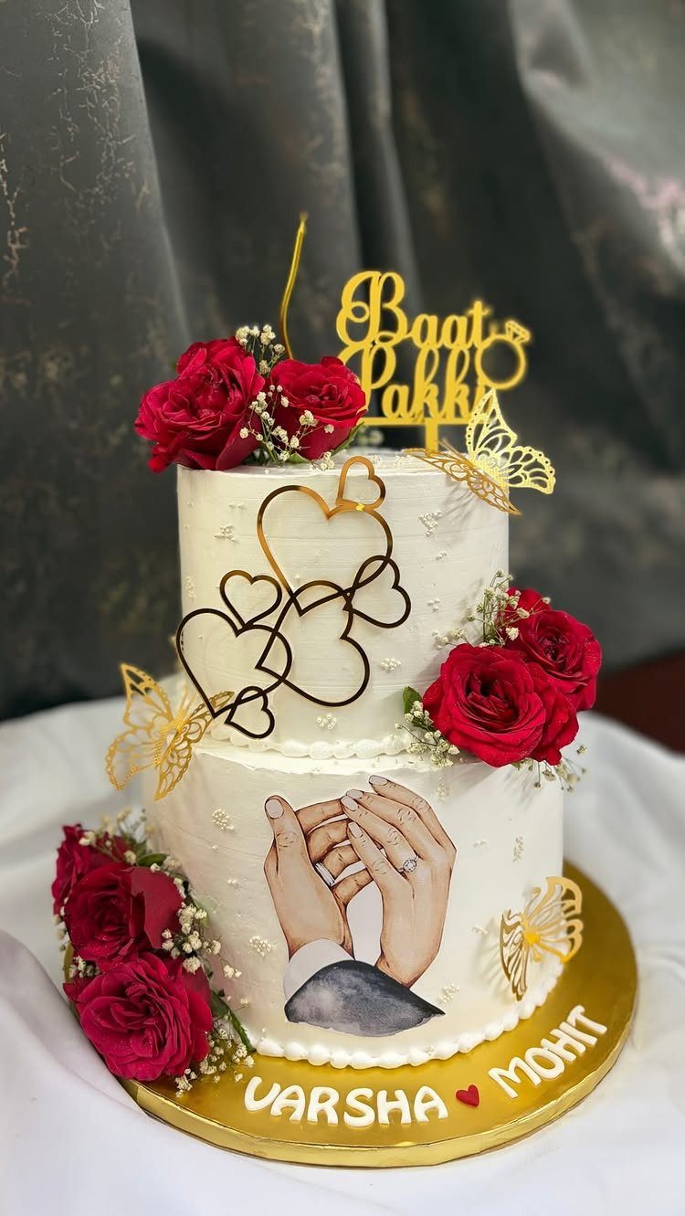 Two-tier white engagement cake with red roses, gold hearts, and a couple's hands image.