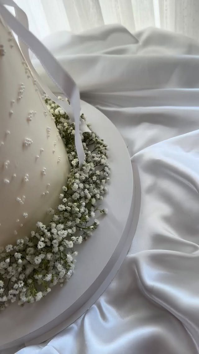 White frosted cake with baby's breath flowers on white satin fabric