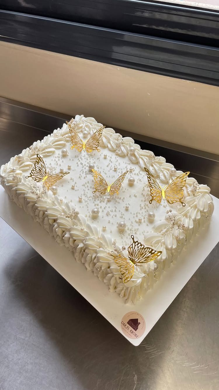White rectangular cake with gold butterfly toppers and pearl decorations on white board.