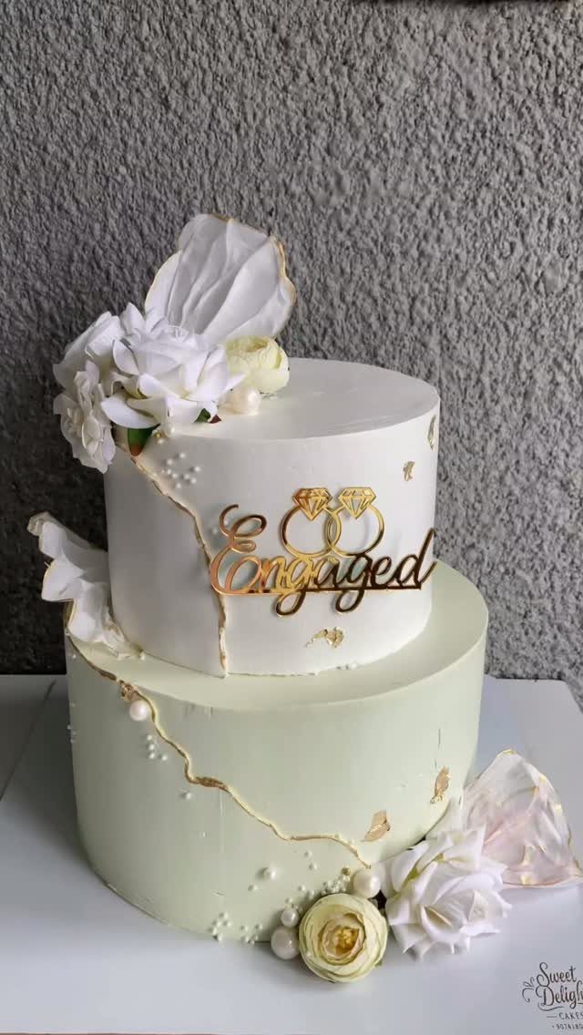 Two-tier white and green cake with gold foil accents and Engaged topper.