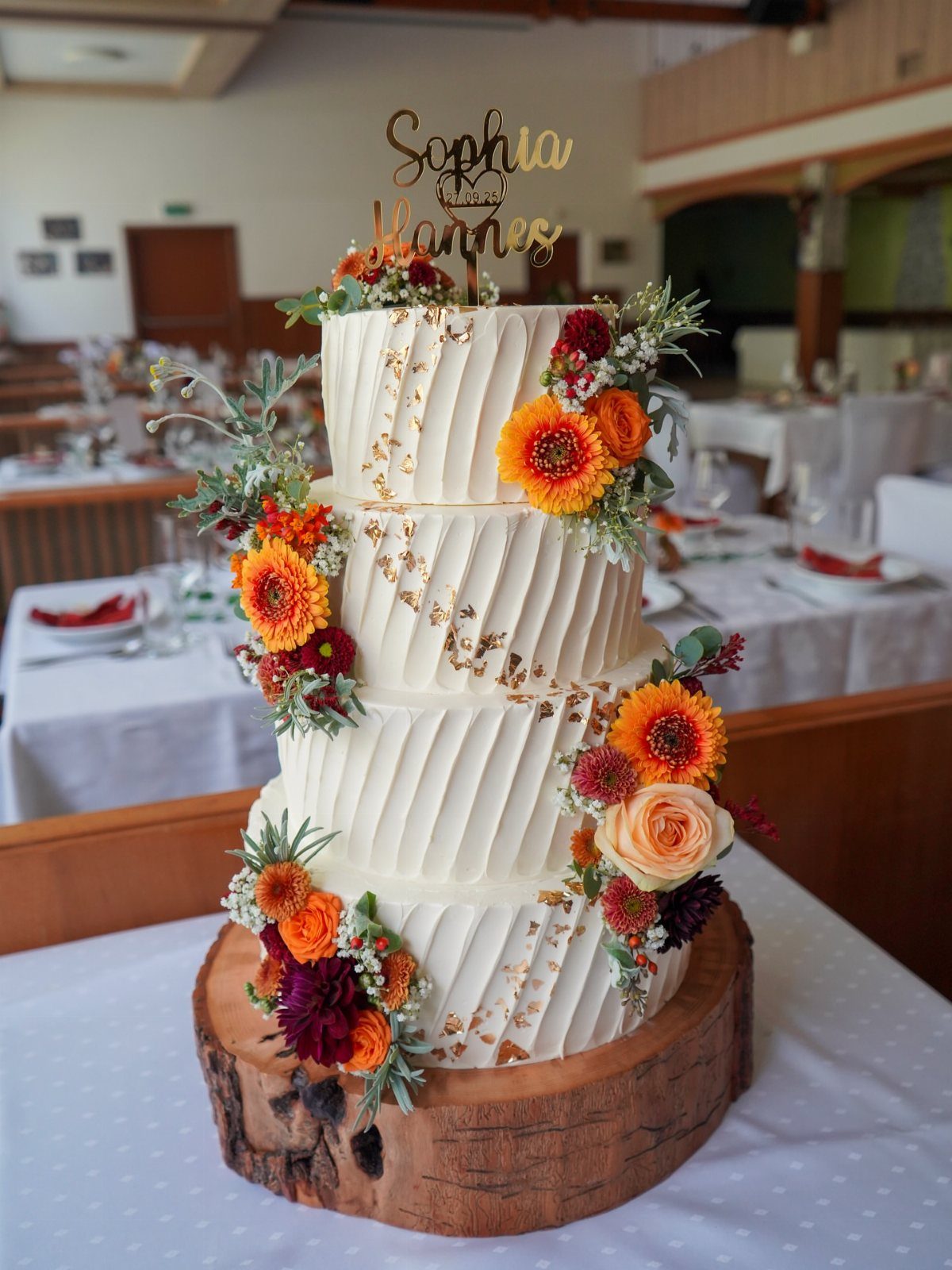 Three-tier white wedding cake with autumn flowers on a rustic wooden log base.
