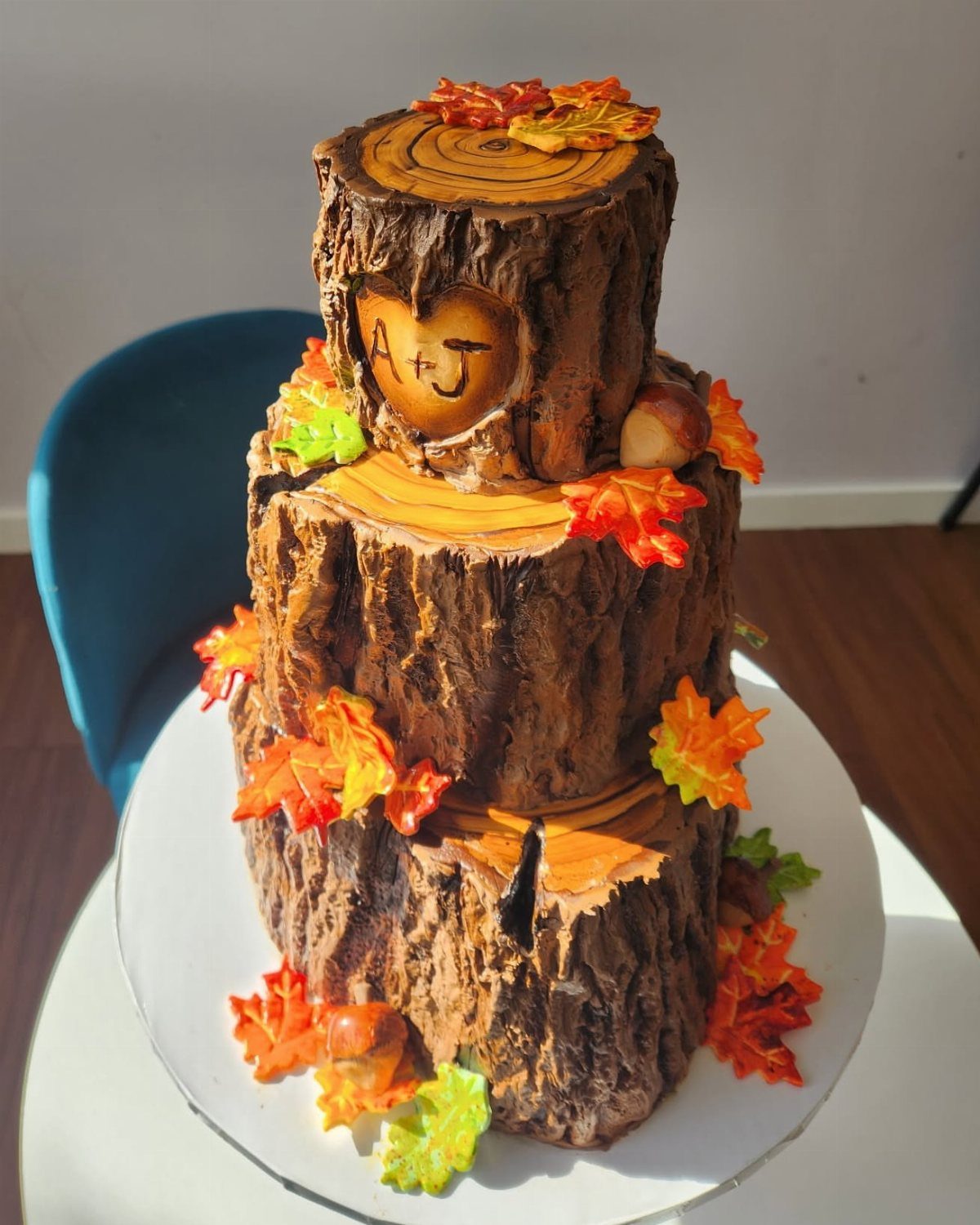 Three-tier tree log wedding cake decorated with autumn leaves and carved heart initials.
