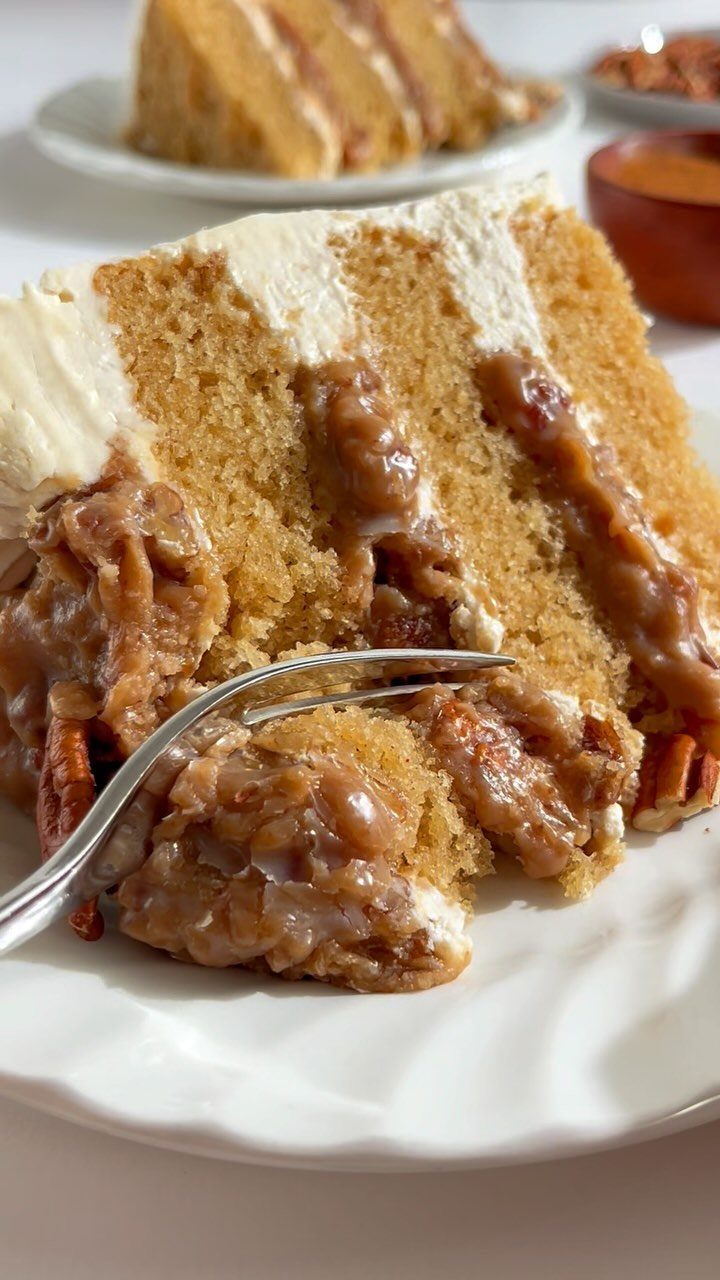 Slice of layered spice cake with caramel pecans and white frosting on plate