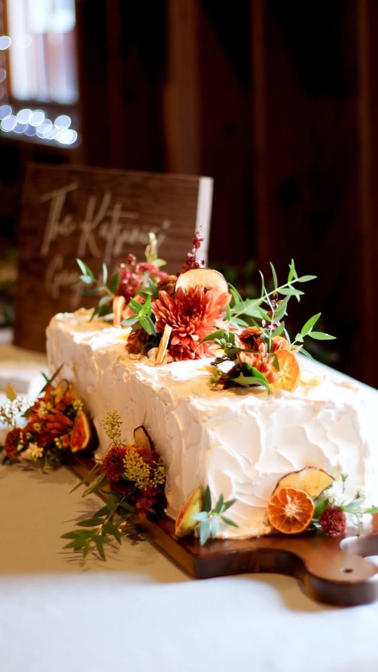 White frosted cake decorated with autumn flowers and dried orange slices on wood.