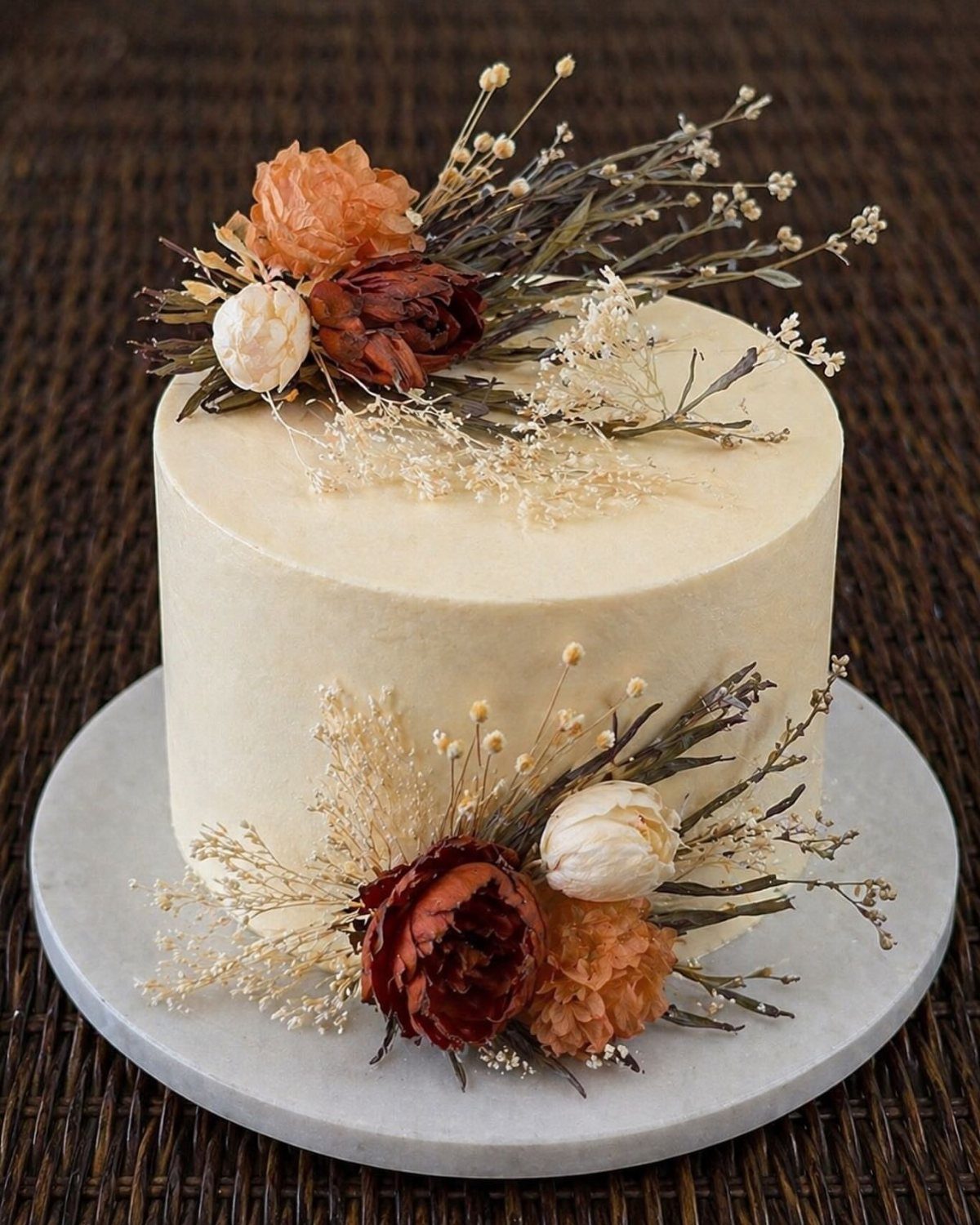 White frosted cake decorated with dried orange and burgundy flowers and foliage.