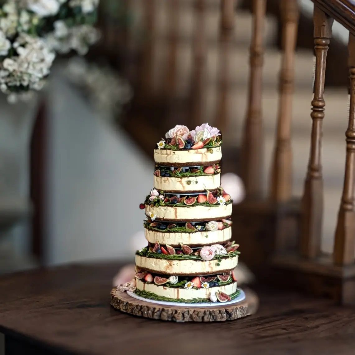 Multi-tiered naked cake decorated with fresh sliced figs, blueberries, and pink flowers.
