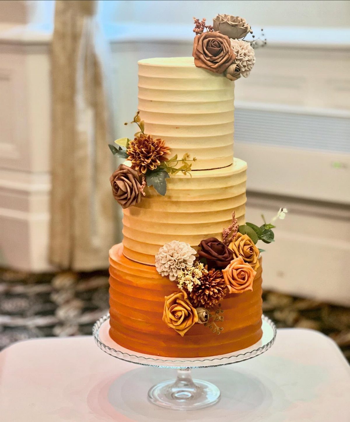 Three-tier ombre wedding cake transitioning from cream to orange with autumn floral decorations.
