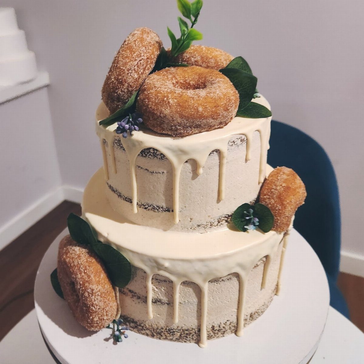 Two-tier semi-naked cake decorated with cinnamon donuts, white drip, and green foliage.