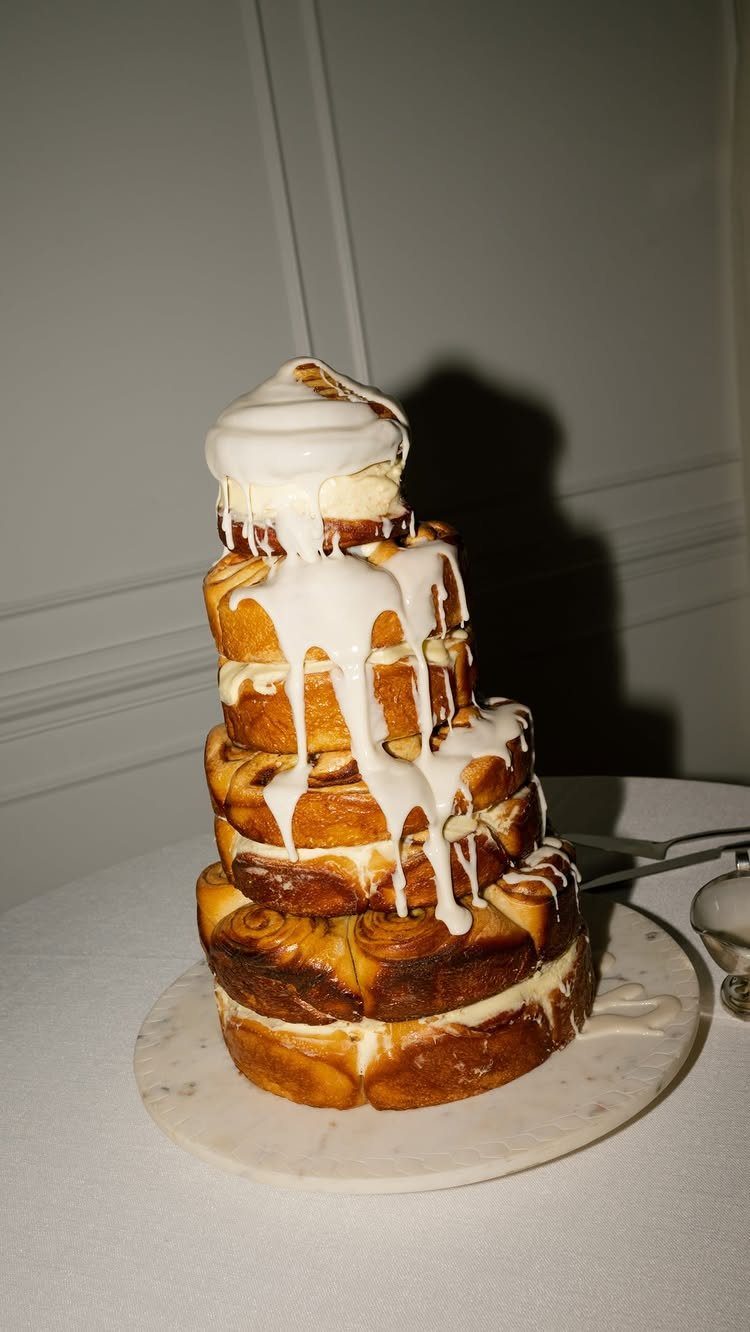 Tiered cinnamon roll cake with white icing dripping on a marble platter.