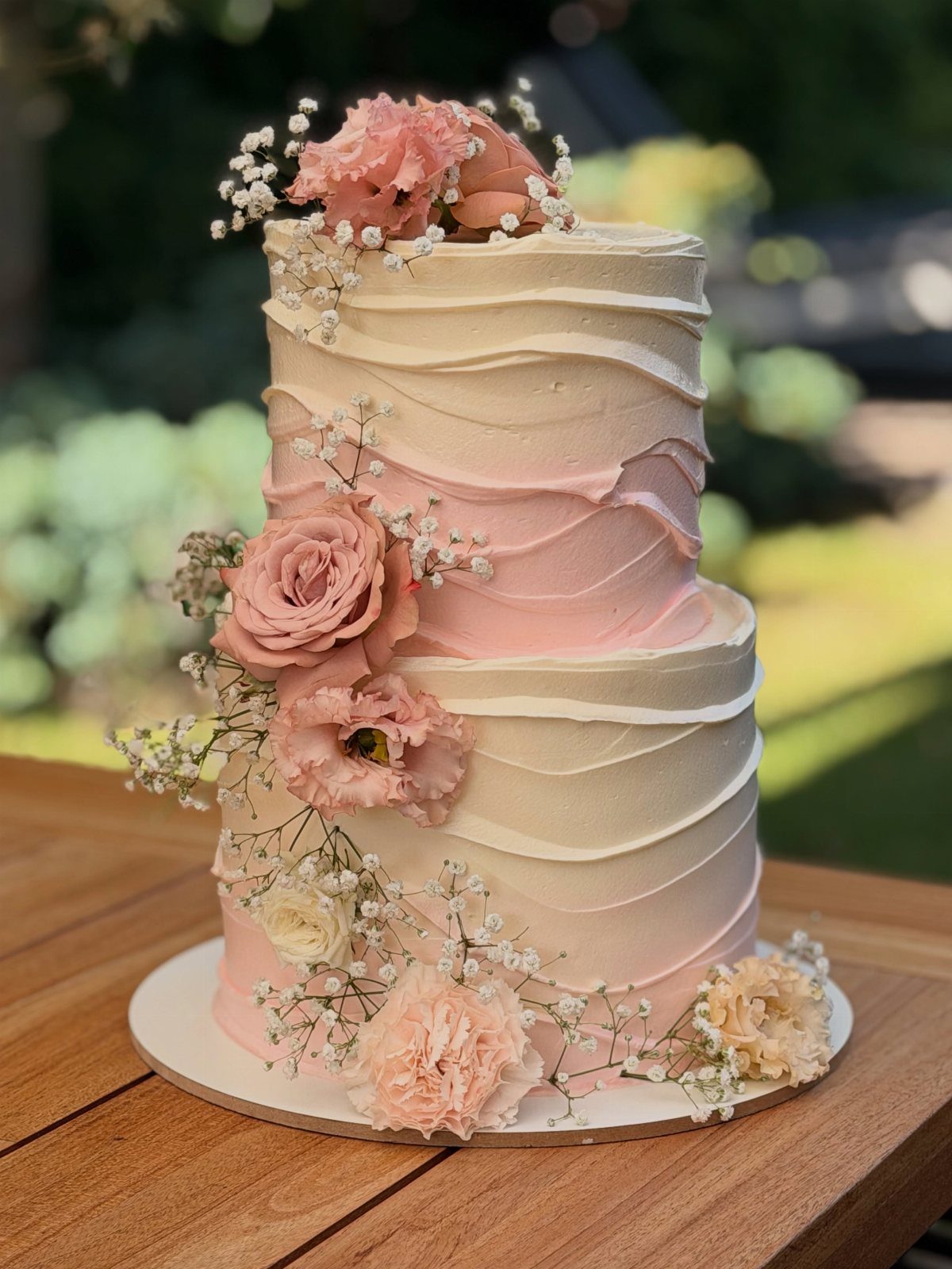 Two-tier wedding cake with pink and white textured frosting and fresh floral decorations.
