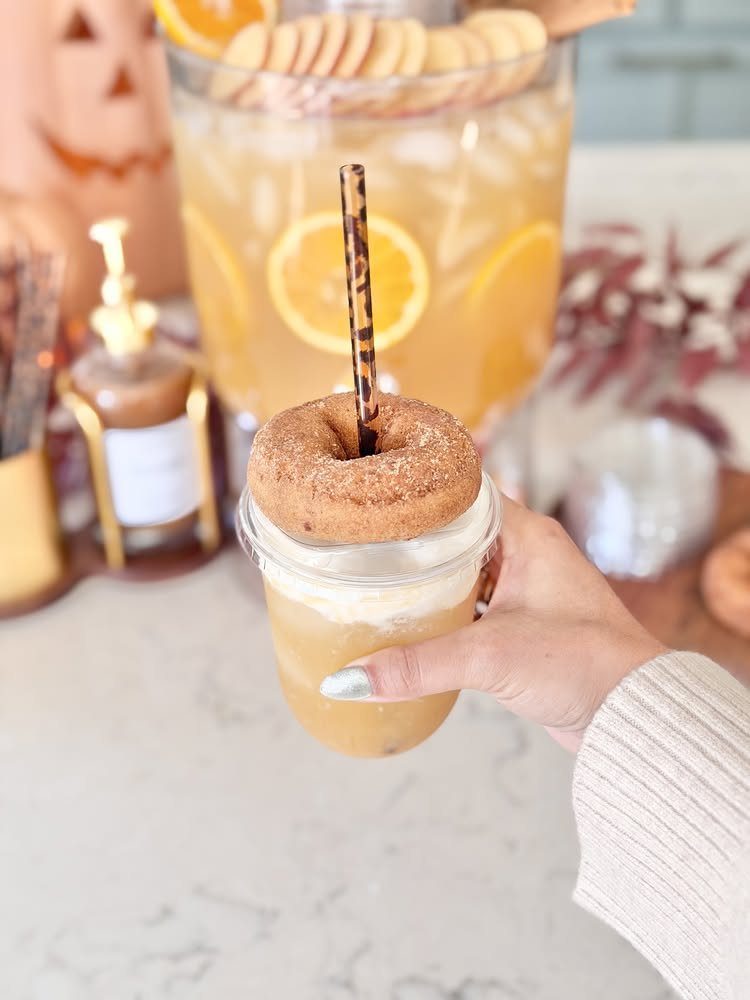Iced apple cider drink topped with a cinnamon donut and leopard-print straw.