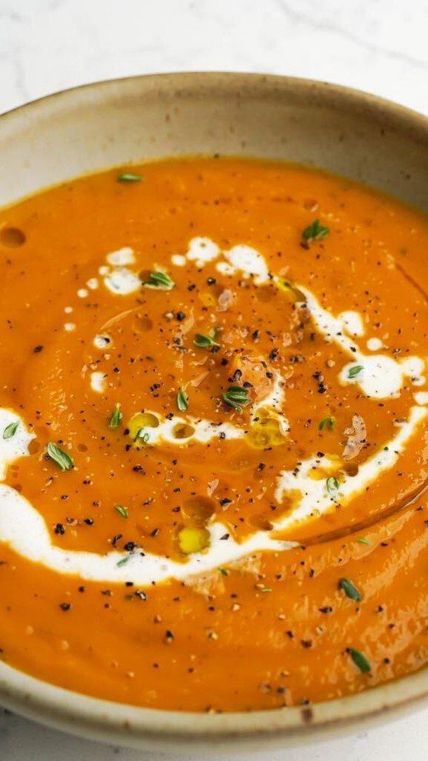 Creamy orange butternut squash soup with cream swirl and fresh green herbs.