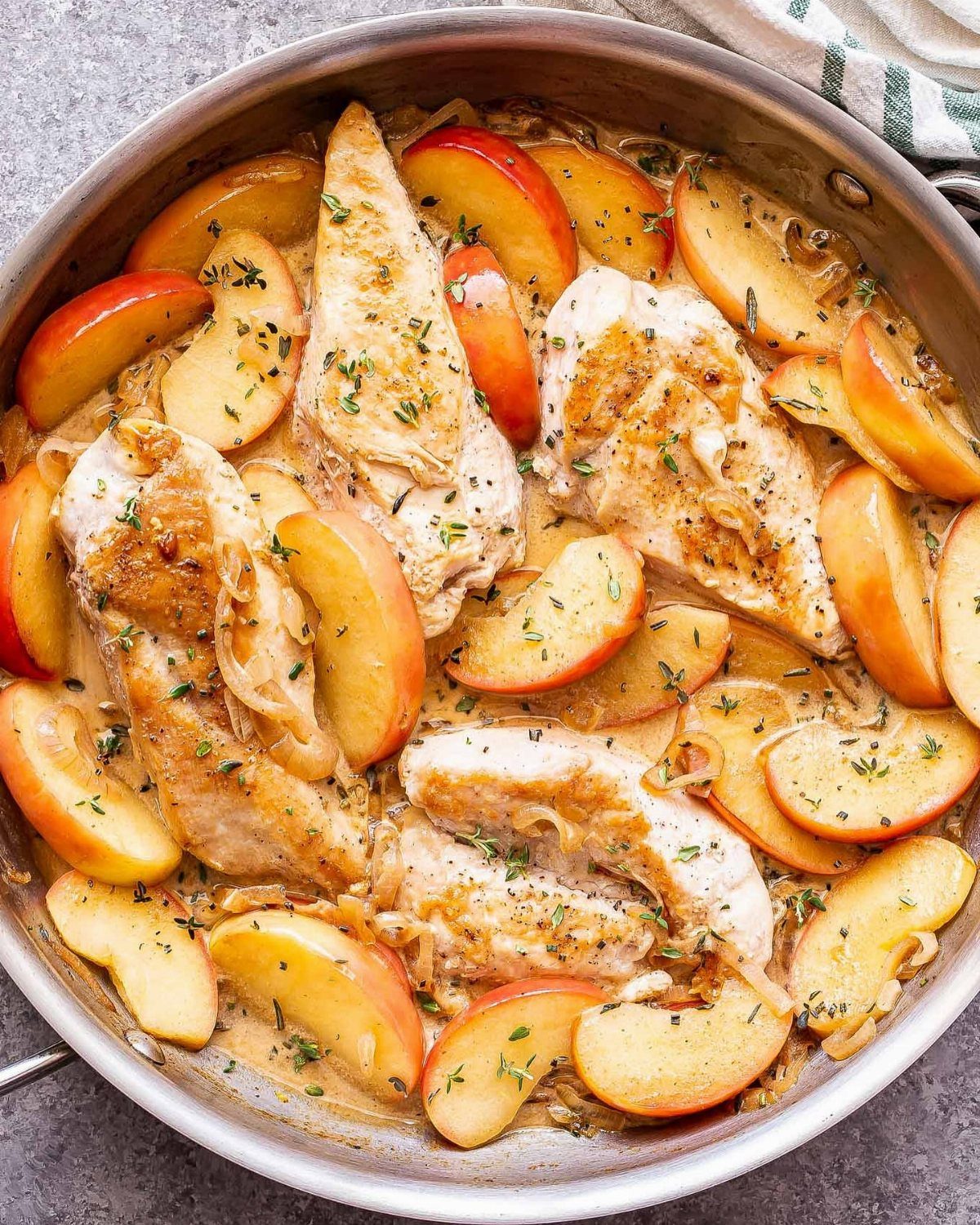 Chicken breasts and apple slices braised in a skillet with fresh herbs.
