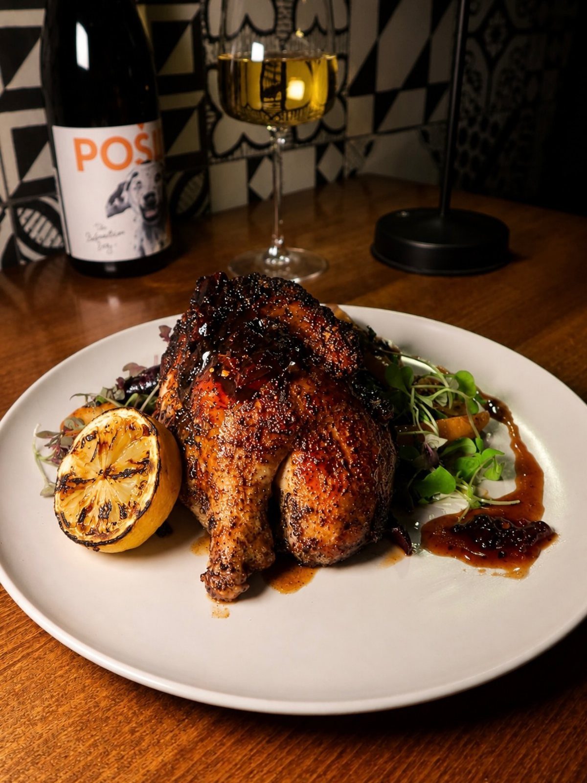 Roasted Cornish game hen with grilled lemon and salad on a white plate.
