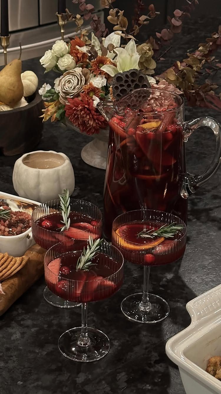 Red sangria with orange slices and rosemary in a pitcher and glasses.