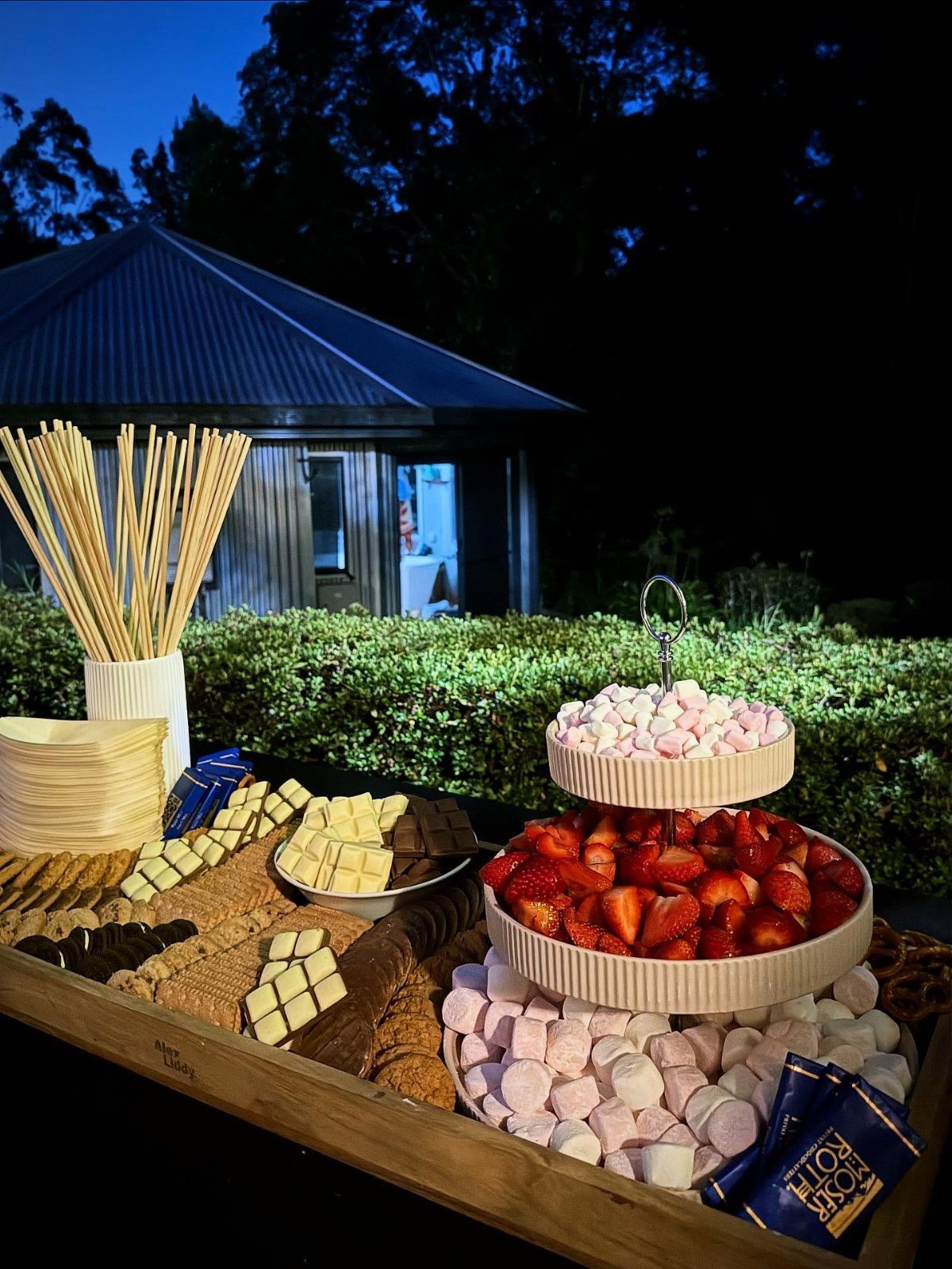 S'mores bar with marshmallows, strawberries, chocolate, and crackers on a wooden board.