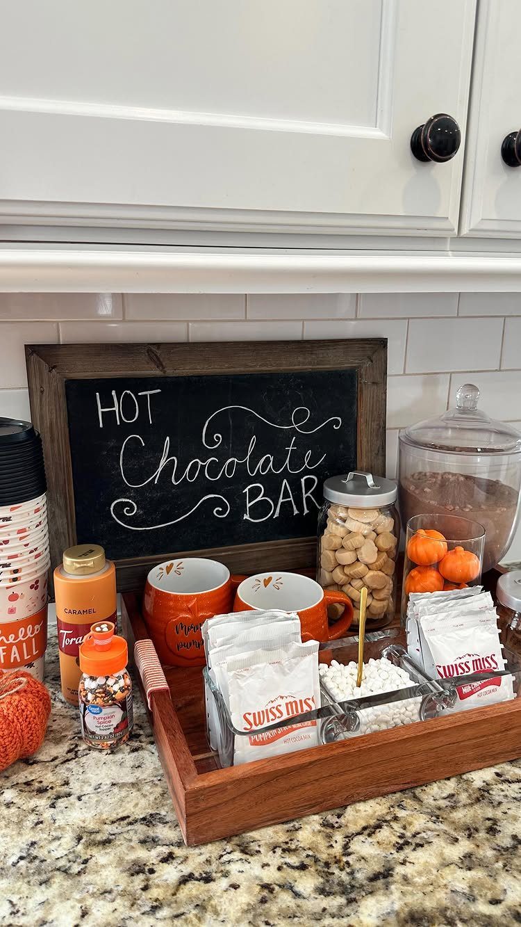 Hot chocolate bar with orange mugs, cocoa packets, and marshmallows on a tray.