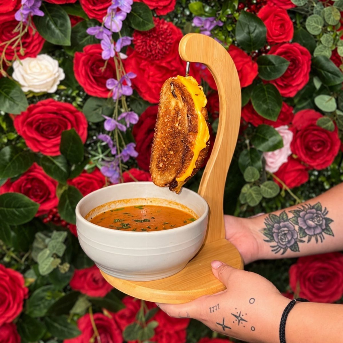 Mini grilled cheese sandwich hanging over a bowl of tomato soup with roses.