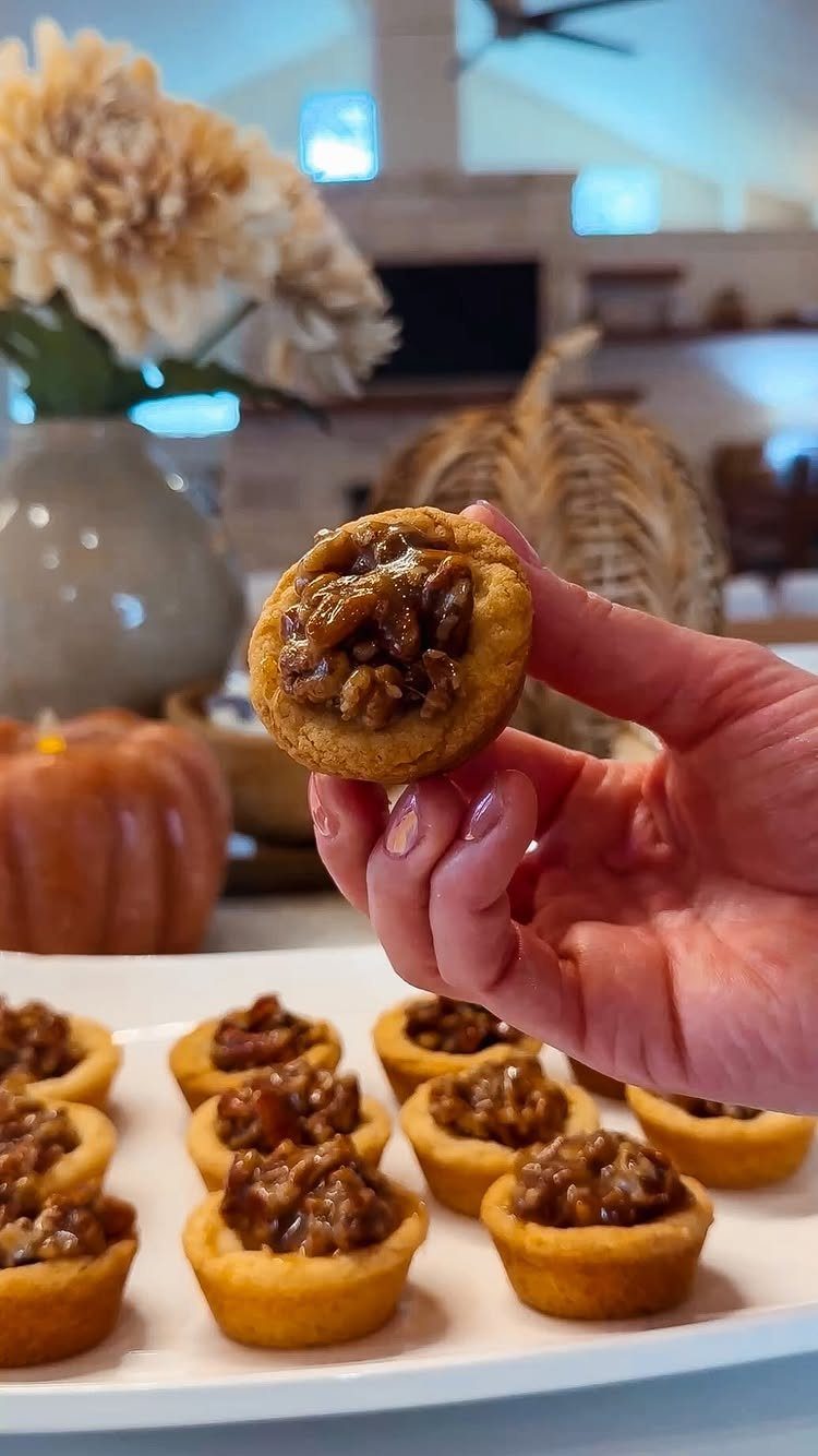 Small pecan pie bites on a white platter with pumpkins in the background.
