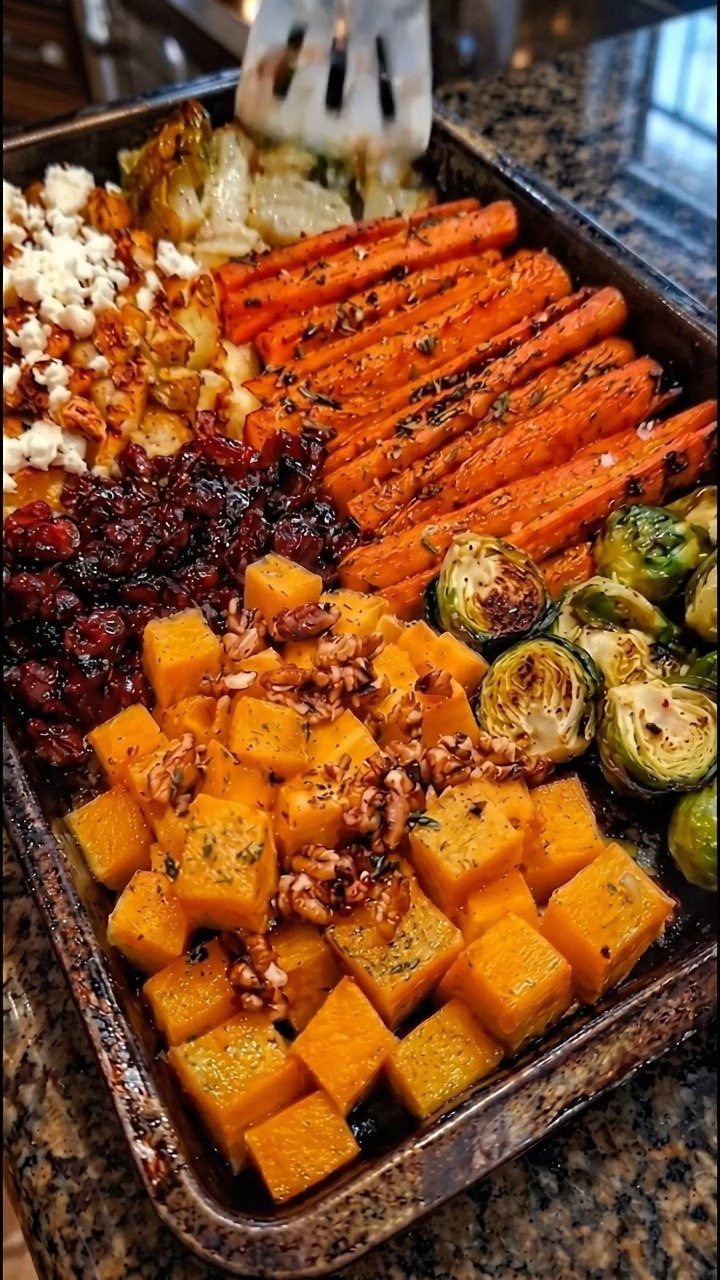 Roasted autumn vegetables including carrots, squash, and Brussels sprouts on a baking sheet.