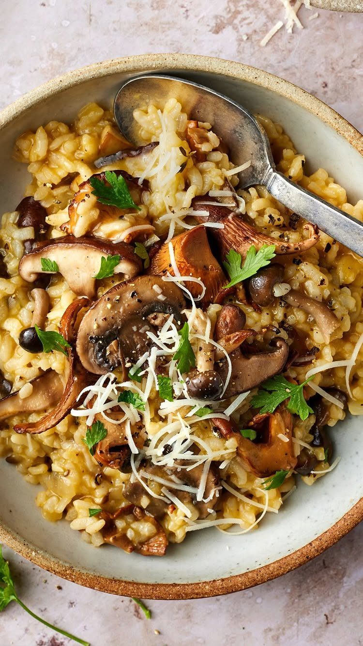 Mushroom risotto in a bowl topped with sliced mushrooms, shredded cheese, and parsley.