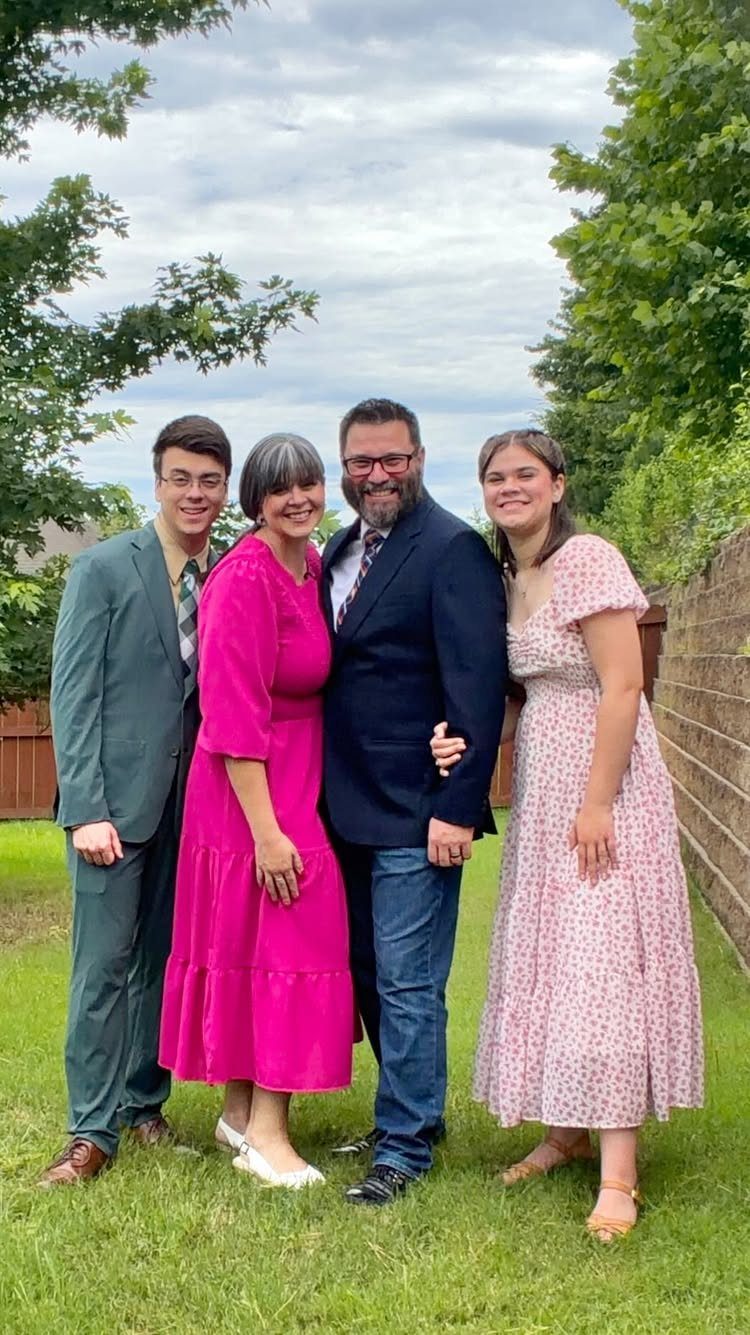Family of four posing outdoors in semi-formal pink and green attire on grass.