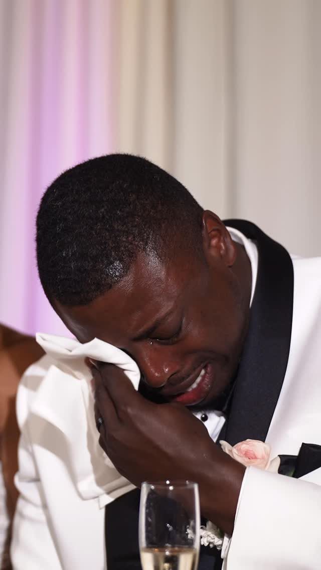 Emotional man in white tuxedo wiping tears with a cloth at a wedding